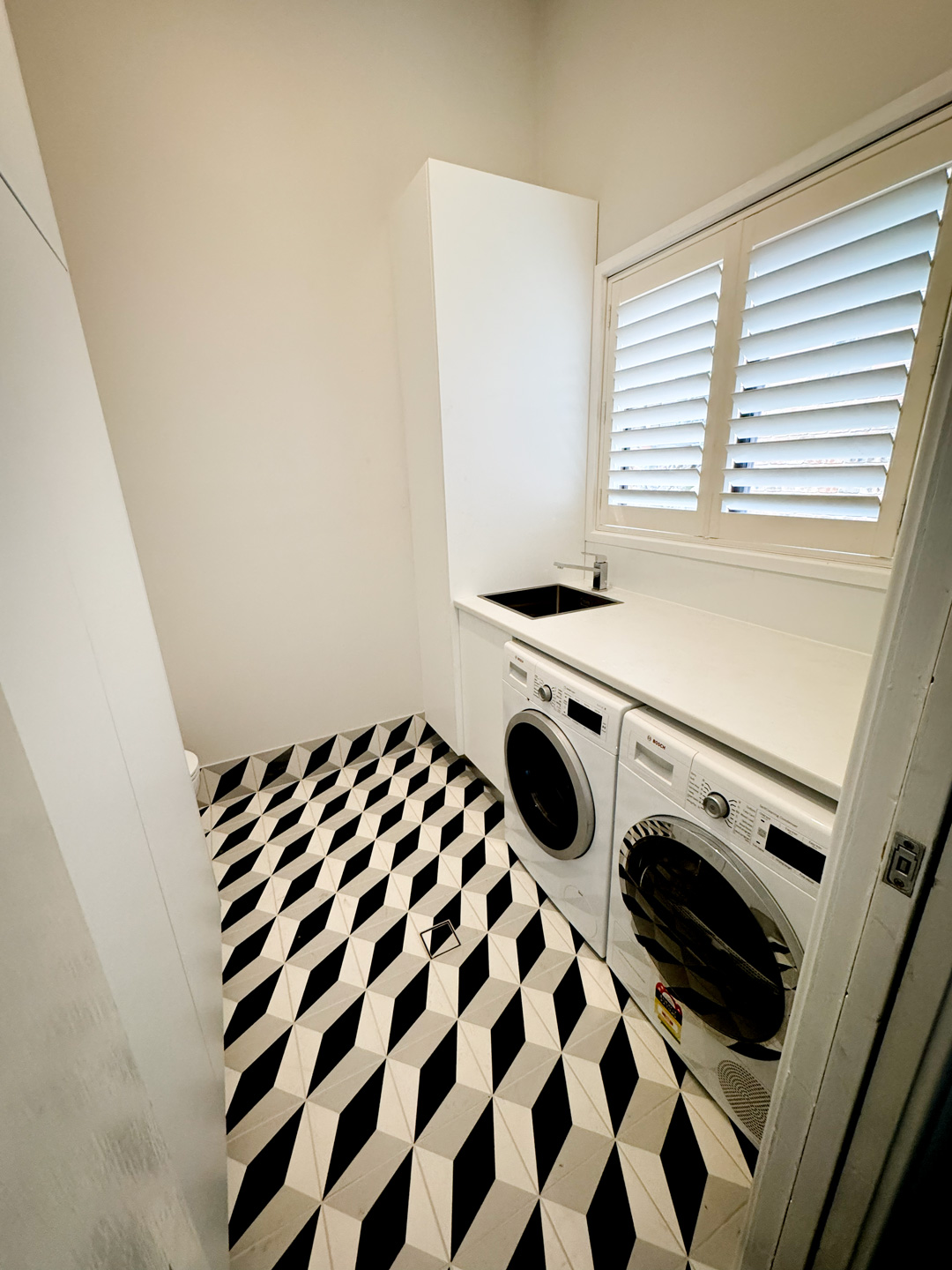 A laundry room with a bold black, white, and grey geometric 3D-patterned tile floor