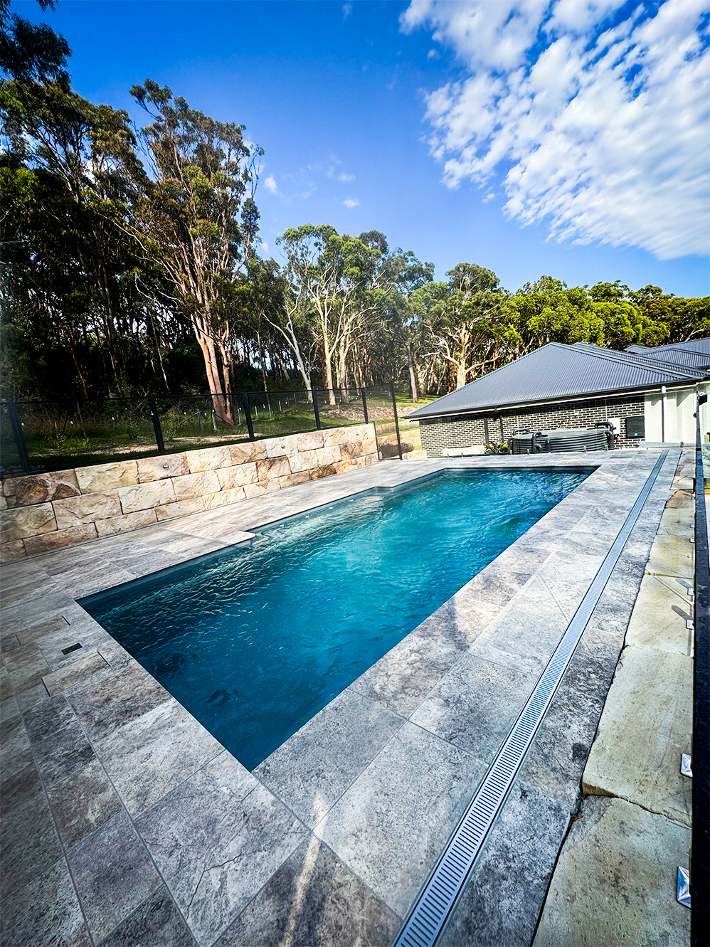 An outdoor rectangular swimming pool with turquoise water, surrounded by grey stone tiling.