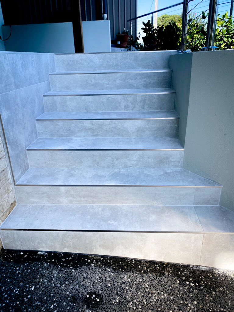 Outdoor stairs with light grey stone-look tiling and silver metal nosing
