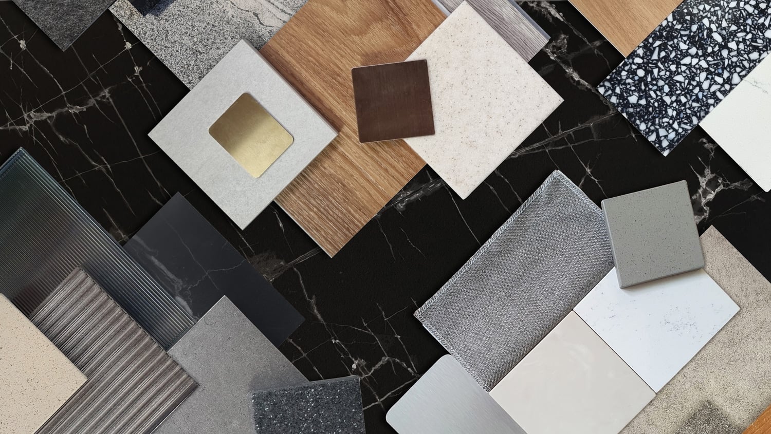 A flat-lay arrangement of various interior design material samples scattered across a black marble background with white veining.