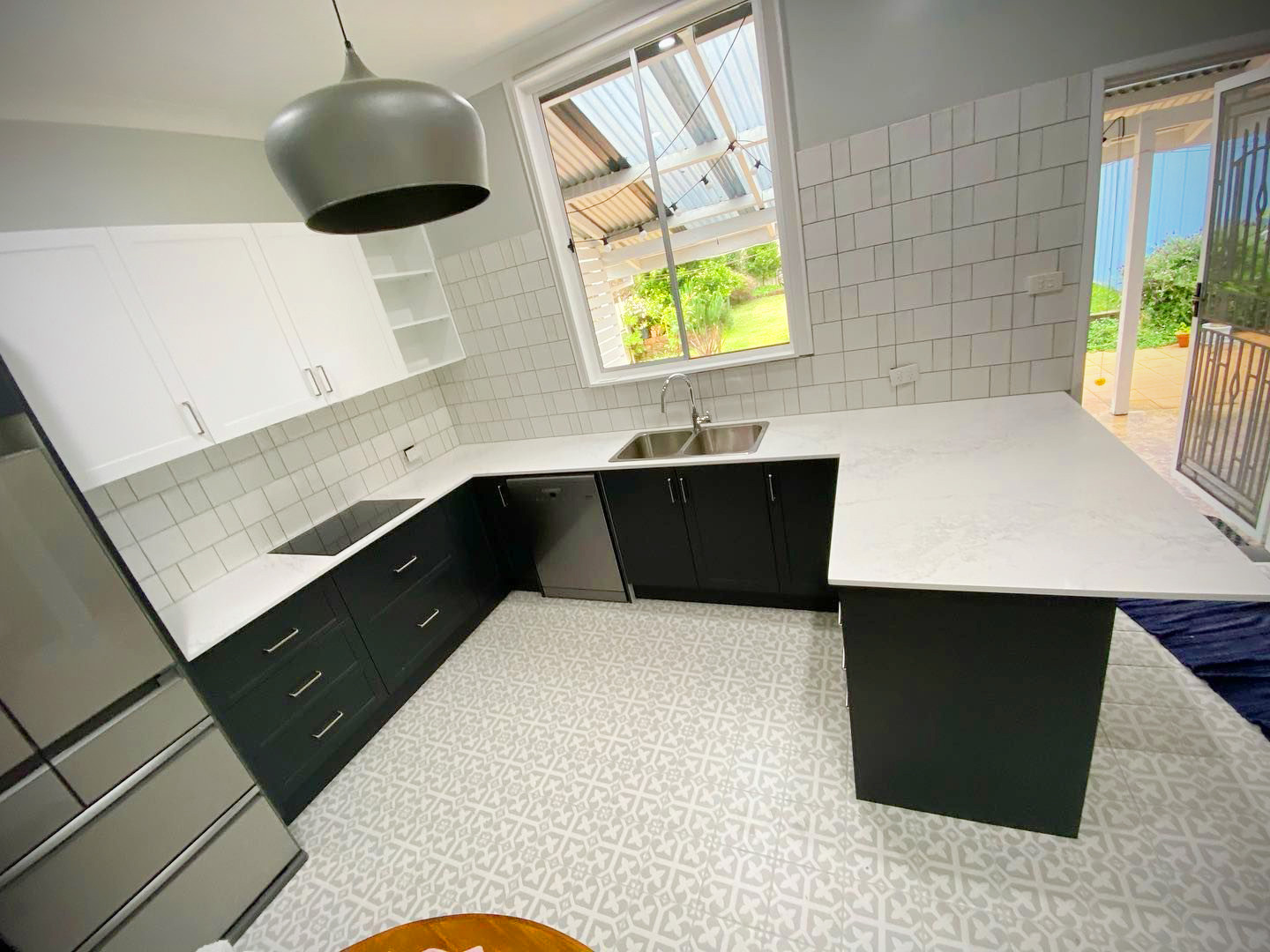 Modern U-shaped kitchen featuring dark charcoal lower cabinets, white upper cabinets, a white marble-patterned countertop, and patterned grey and white floor tiles.