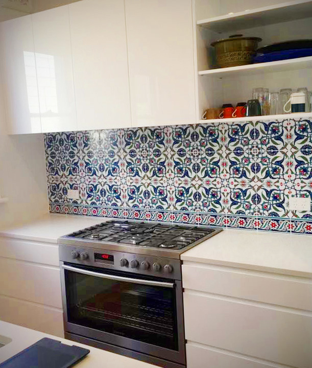 A bright, contemporary kitchen with white cabinetry, countertops and a vibrant blue and red patterned tile backsplash that adds a decorative Mediterranean.