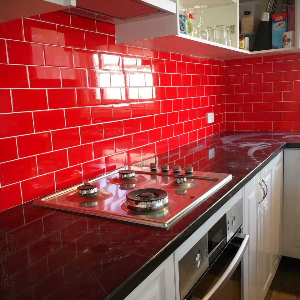 A modern kitchen featuring a vibrant bright red subway tile backsplash and a dark maroon countertop.