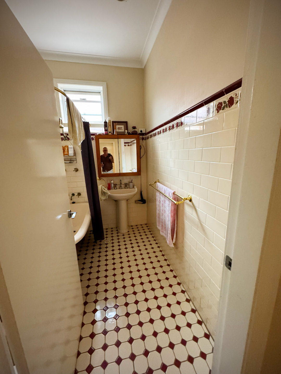 A vintage bathroom with cream subway tiles on the right wall and a patterned floor of white and burgundy octagonal tiles.