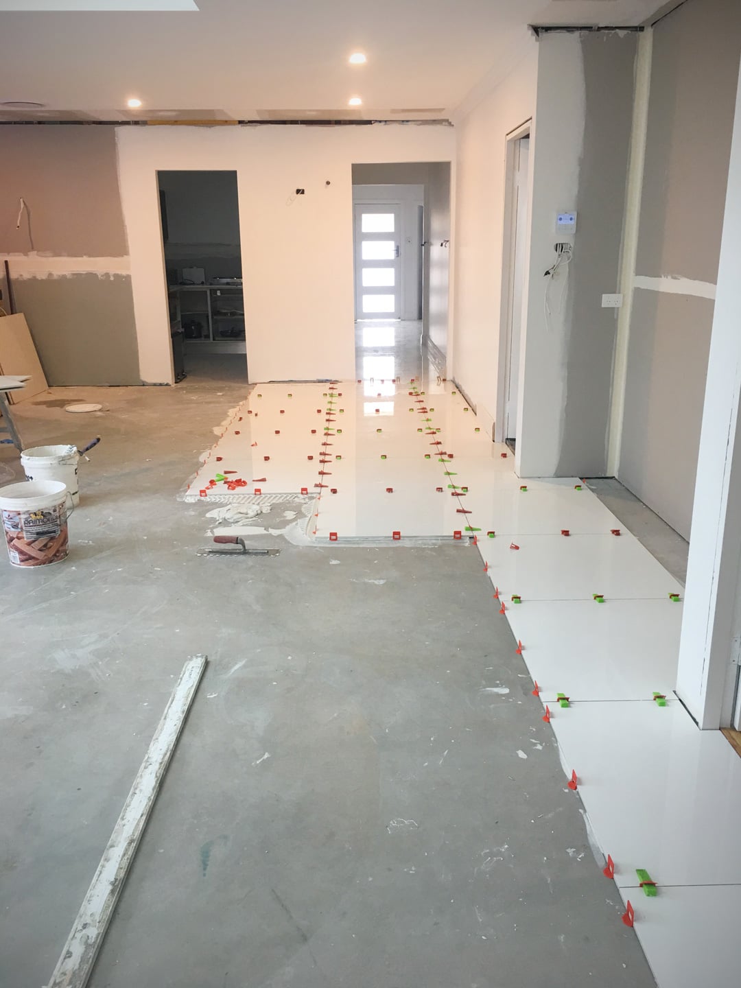 A high-angle shot of a room under renovation, showing the progress of laying large, white, glossy floor tiles.