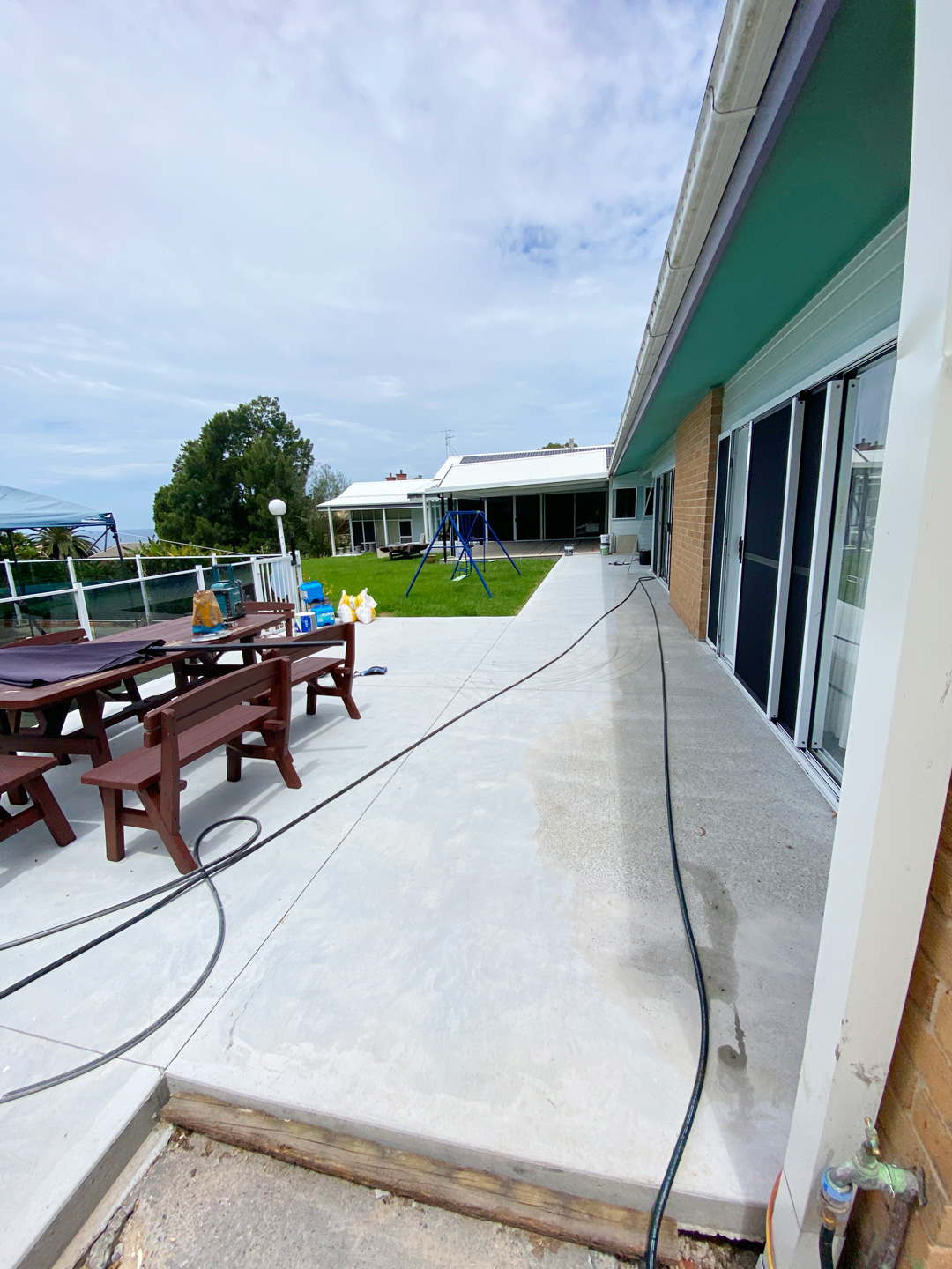A light grey concrete patio running alongside a house with large sliding glass doors and a teal soffit.