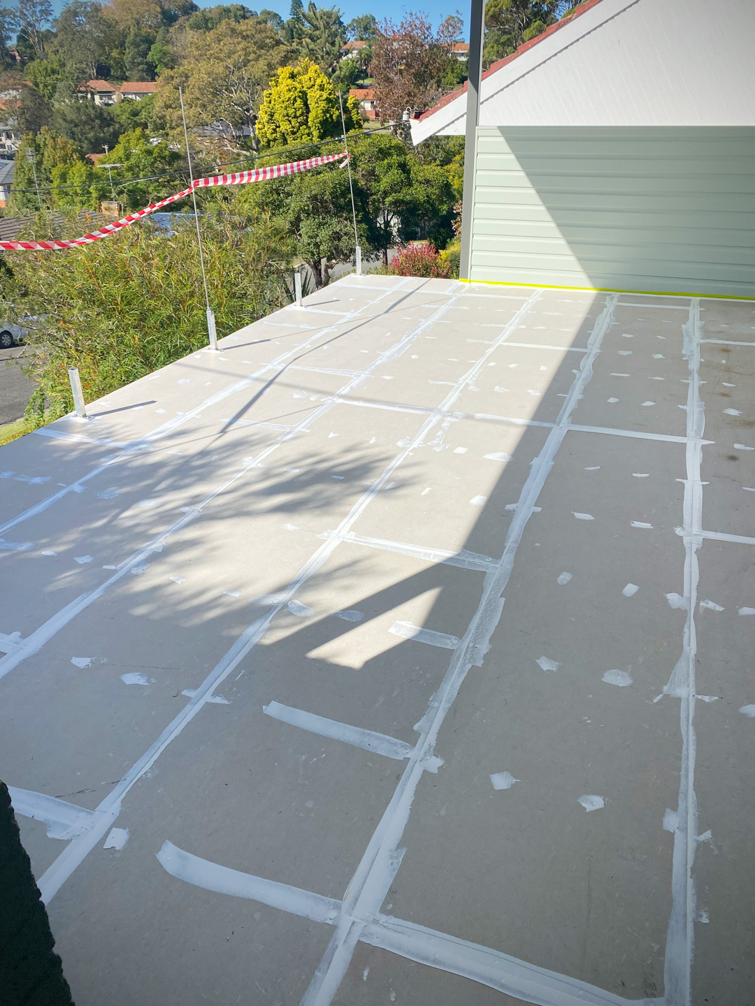 The finished outdoor patio featuring light-coloured, rectangular tiles laid in a running bond pattern alongside a light green house wall with a white sliding door.