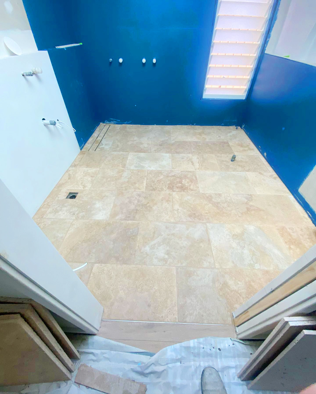 A bathroom under renovation with beige stone floor tiles and vibrant deep blue waterproofed walls.