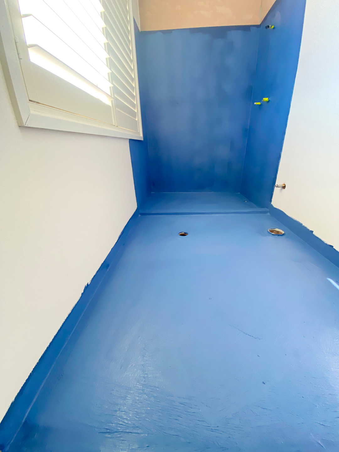 A bathroom renovation in progress, showing a floor and lower wall section coated in a bright blue waterproofing membrane.