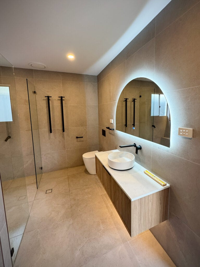 A completed modern bathroom featuring large-format beige tiles on the floors and walls.